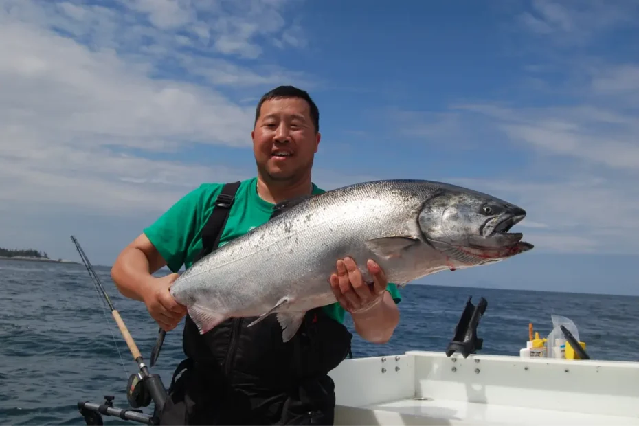 An angler smiling and holding a massive chrome Chinook salmon caught while executing an elite downrigger trolling strategy on a sportfishing boat.