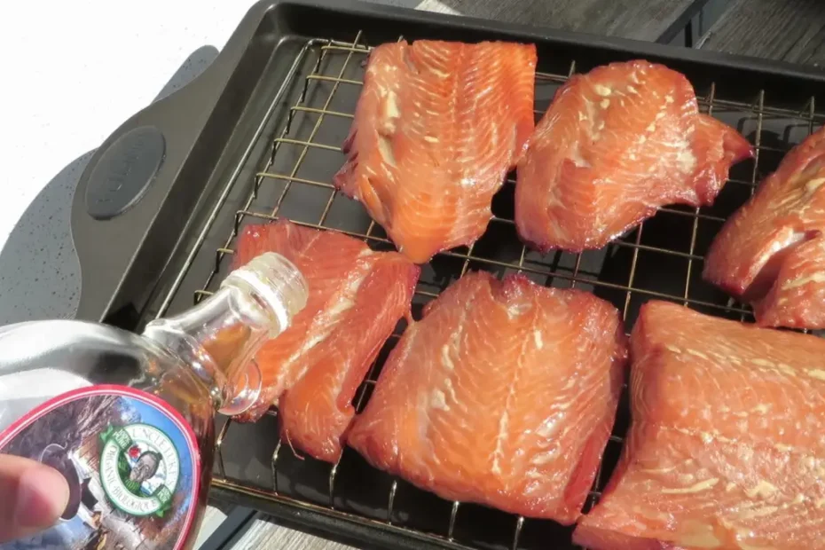 Pouring pure maple syrup glaze over smoked salmon fillets on a wire smoking rack.