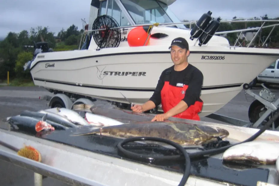 Angler standing at a marine cleaning station prep table with fresh Pacific salmon and halibut, featuring a white Seaswirl Striper sportfishing boat on its trailer in the background.